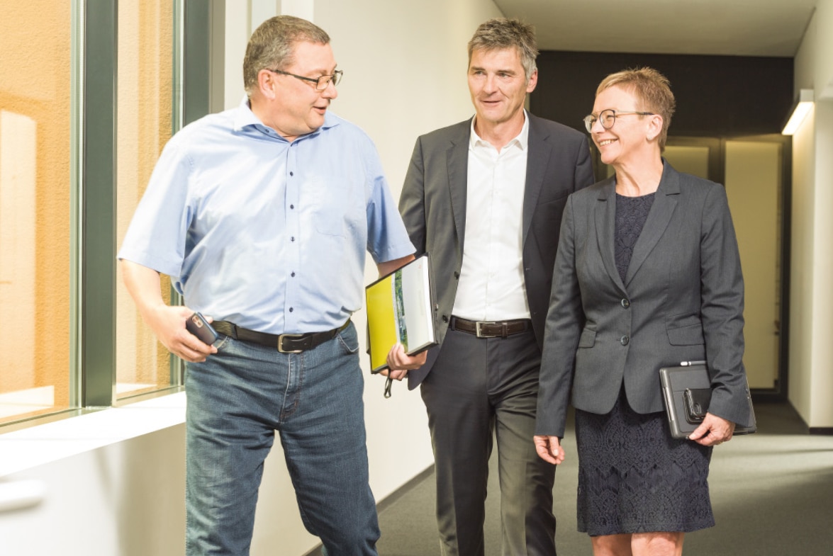 Symbolbild mit zwei Männern und einer Frau im Business-Look, die dem Betrachter entgegenkommen.